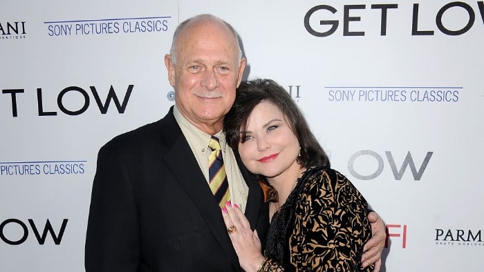 Gerald McRaney wearing black suit with a yellow tie.